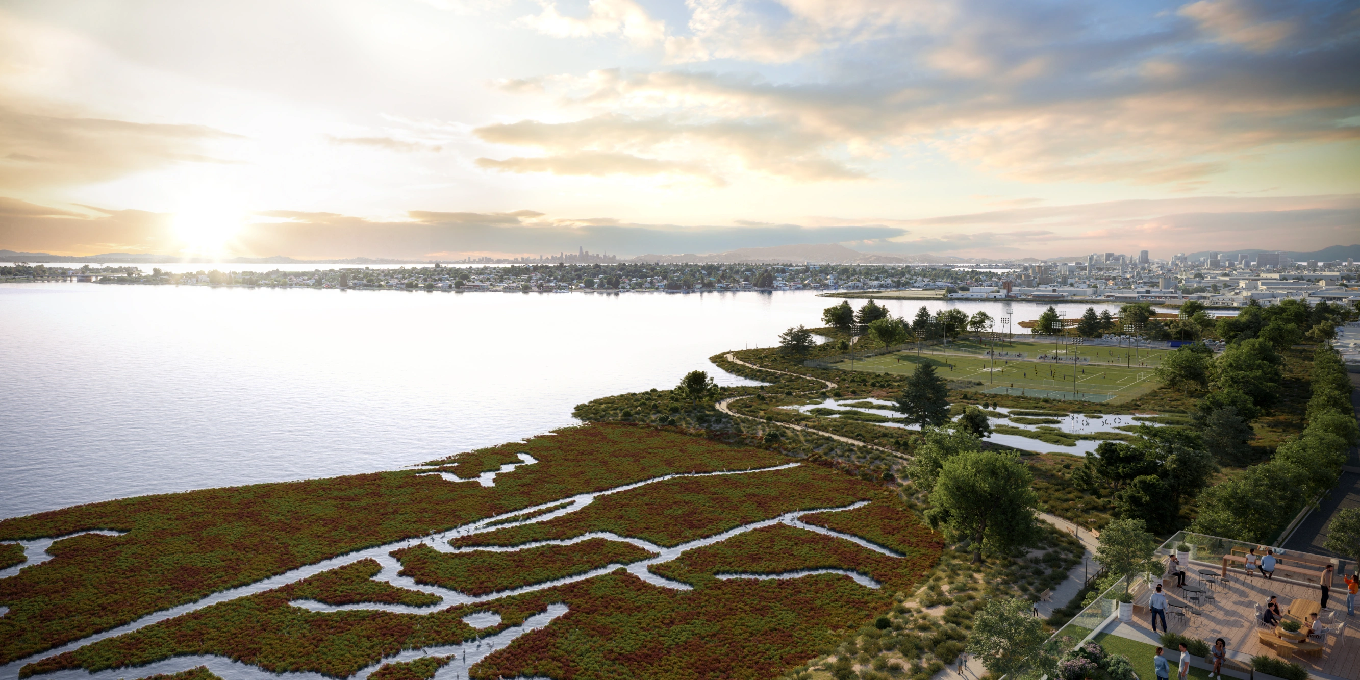 Waterfront marshland at sunset with urban skyline and sports fields